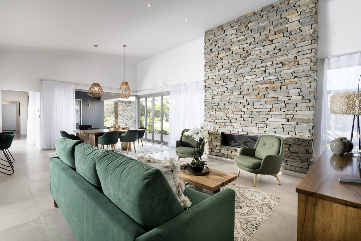 Elegant open-plan living area with full-height stone fireplace and outdoor views, featured in premium corner block house designs.